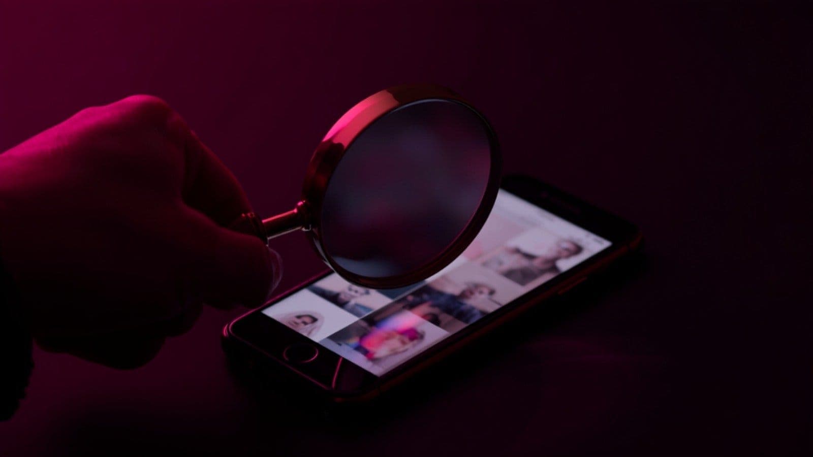 A magnifying glass resting on a phone screen showing a social media profile grid, illustrating the manual check an Indian brand can run to spot an influencer's fake followers before paying for a campaign