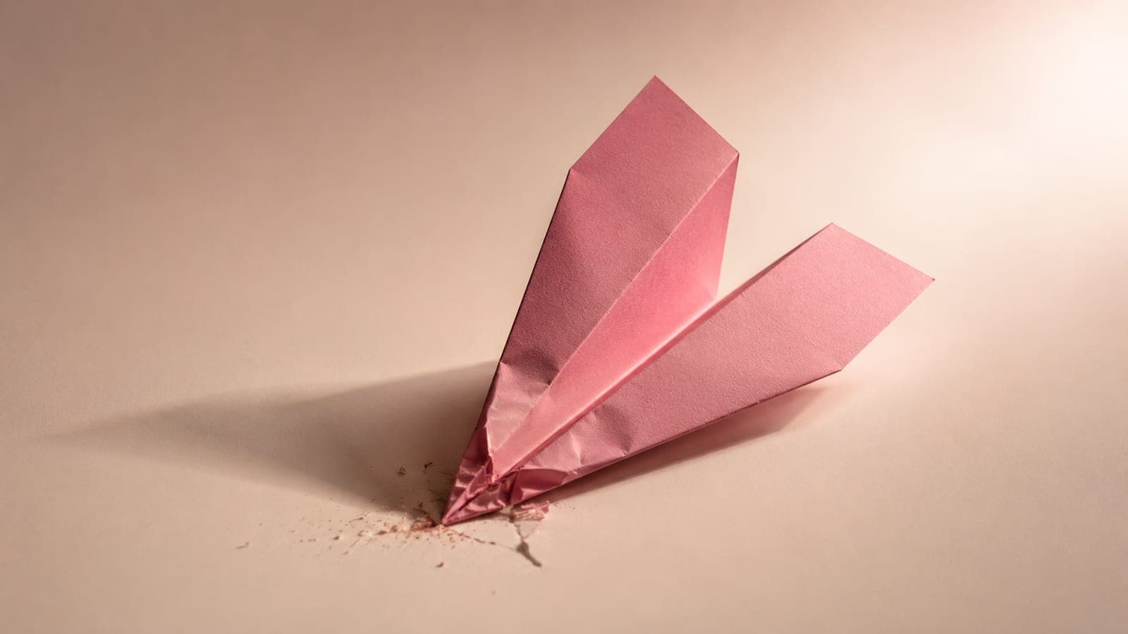 A pink paper airplane crashed onto a clean white surface, photographed from a low angle