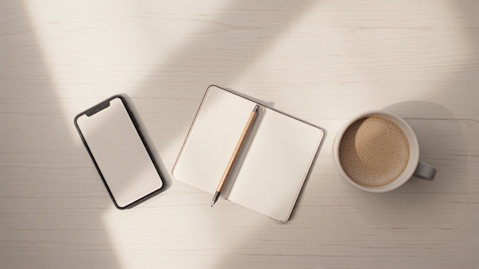 A phone with a blank screen lying beside an open notebook and a cup of coffee on a pale wooden desk, illustrating the messages where Indian creators negotiate brand deal rates and terms