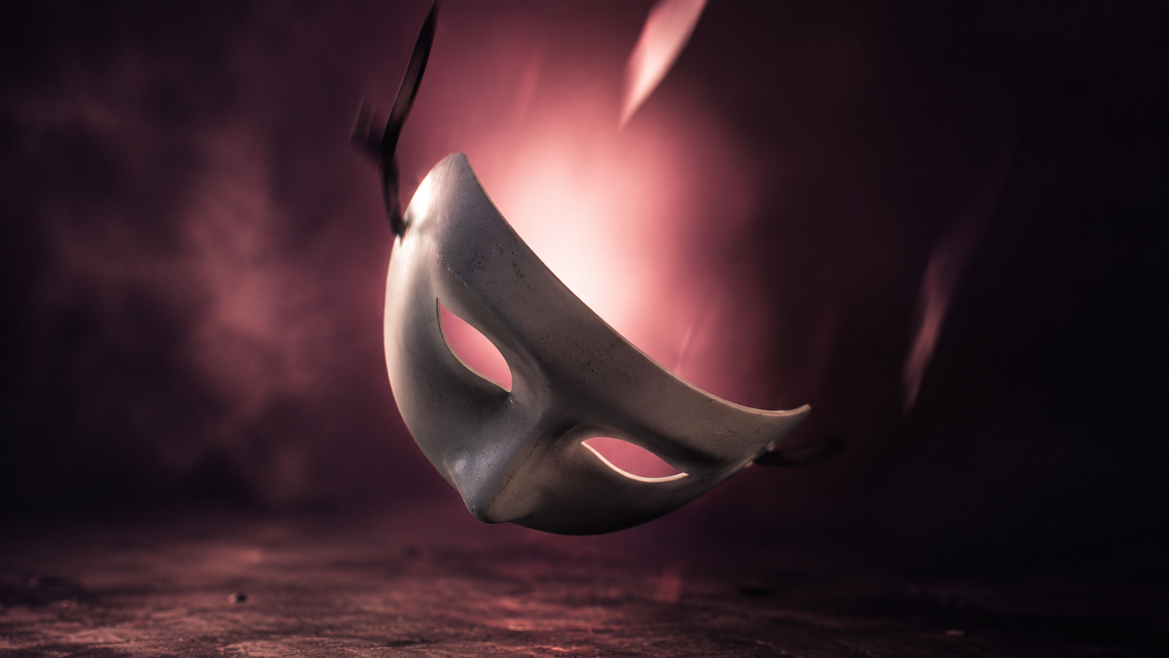 A theatrical mask falling away from a darkened studio backdrop, revealing soft pink light behind it