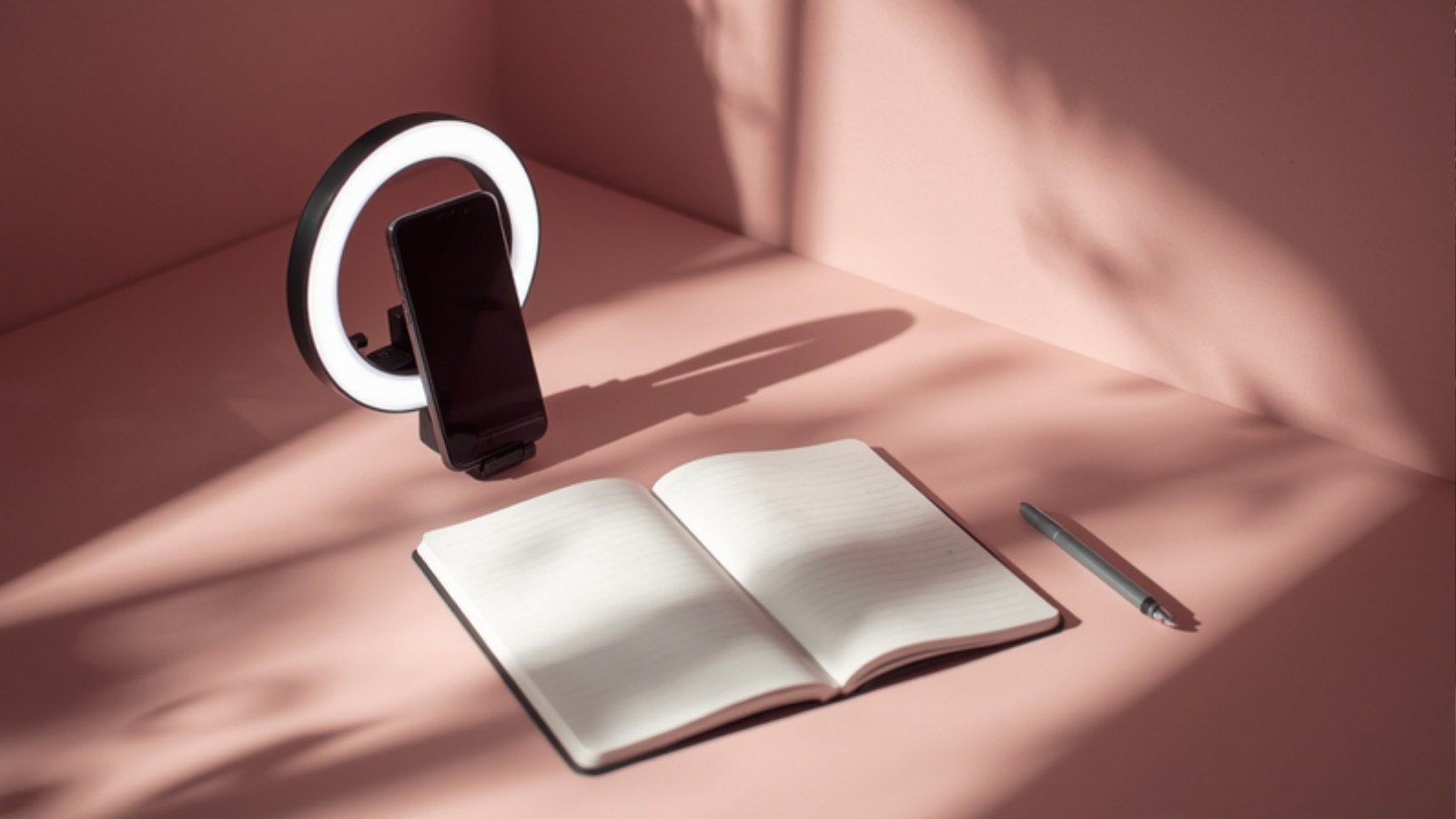 A phone propped on a ring light beside a notebook on a soft pink desk, illustrating the small home setup an Indian creator uses to land their first paid brand deals